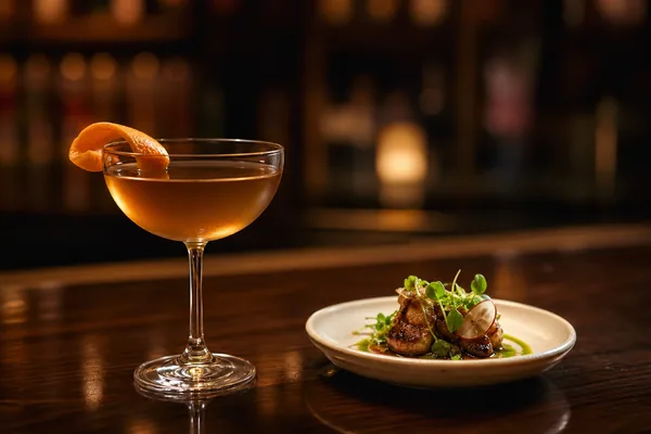 A craft cocktail and plated dish at a dark bar